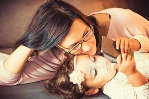 Happy mother and daughter watching cartoons on smart phone. photo