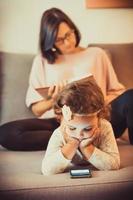 niña pequeña que usa un teléfono inteligente mientras se relaja en el sofá con su madre. foto