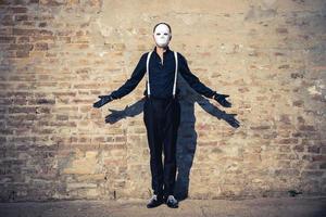 hombre misterioso con máscara blanca contra la pared de ladrillo. foto