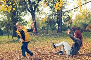 juguetona madre e hijo divirtiéndose con hojas de otoño. foto