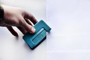 Green hole punch in hand on a white background. Stationery close-up. photo