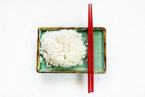 boiled rice and red chopsticks on plate on white photo