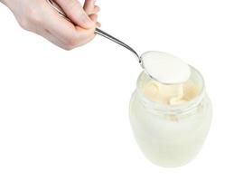 white honey in steel spoon over glass jar isolated photo