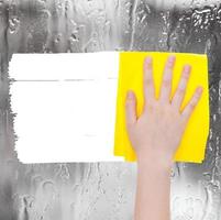 hand deletes rainy water on window by yellow rag photo