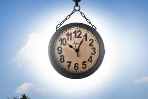 Closeup vintage hanging clock, blurred clouds and bluesky background. photo