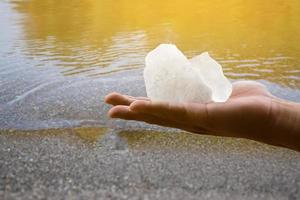 barra de alumbre blanca sosteniendo en la mano con agua turbia, concepto para usar alumbre para balancear o balancear el agua turbia para que esté limpia y clara antes de usarla en la vida diaria humana, enfoque suave y selectivo. foto