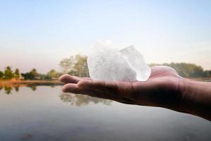 White alum bar holding in hand with cloudy water, concept for using alum to sway or swing the cloudy water to be clean and clear before using it in human daily life, soft and selective focus. photo