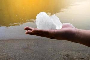 White alum bar holding in hand with cloudy water, concept for using alum to sway or swing the cloudy water to be clean and clear before using it in human daily life, soft and selective focus. photo