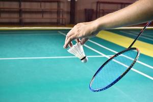 Badminton racket and old white shuttlecock holding in hands of player while serving it over the net ahead, blur badminton court background and selective focus photo