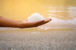 barra de alumbre blanca sosteniendo en la mano con agua turbia, concepto para usar alumbre para balancear o balancear el agua turbia para que esté limpia y clara antes de usarla en la vida diaria humana, enfoque suave y selectivo. foto