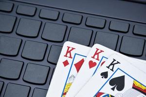 cartas de papel de póquer en el teclado de una computadora portátil en blanco, enfoque suave y selectivo, concepto para jugar cartas en línea con otras personas en casa y actividad recreativa. foto