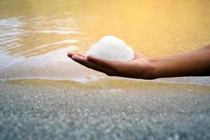 White alum bar holding in hand with cloudy water, concept for using alum to sway or swing the cloudy water to be clean and clear before using it in human daily life, soft and selective focus. photo