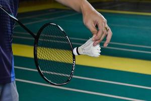 Badminton racket and old white shuttlecock holding in hands of player while serving it over the net ahead, blur badminton court background and selective focus photo