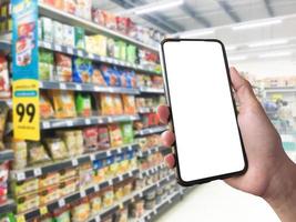 Smart shopping concept mobile phone in hand in front of goods shelves in supermarket and grocery store. blank white screen mockup for your own creativity. photo