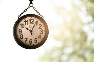 Closeup vintage hanging clock, blurred tree and sunlight background, soft and selective focus on clock. photo