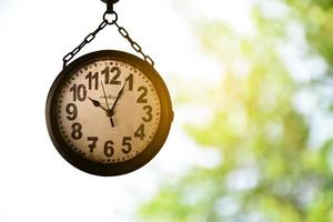 Closeup vintage hanging clock, blurred tree and sunlight background, soft and selective focus on clock. photo