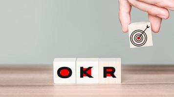 Man holding a wooden cube block with goal icon and OKR or Objectives and Key Results text. Business growth the plan in concept. photo