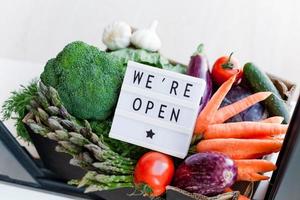 texto que estamos abiertos y caja de verduras y verduras frescas foto