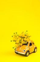 Car toy model delivering bouquet of mimosa flowers photo