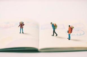 figuras de personas en miniatura con mochila caminando y de pie en la página del pasaporte con sellos de inmigración, concepto de viajes y vacaciones foto