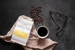 identidad de marca de granos de café y taza caliente de bebida de café negro con anteojos sobre fondo de piedra, concepto de negocio y maqueta foto