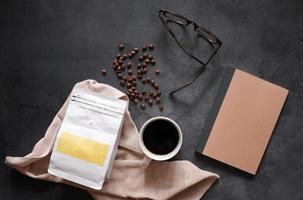 Branding identity of coffee beans and hot cup of black coffee drink with blank notebook on stone background, business and mockup concept