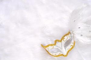 Top view of white fancy mask for party celebration on white soft fur fabric background, holiday and carnival event photo