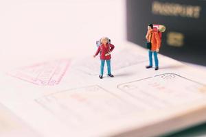 Miniature people figures with backpack walking and standing on passport page with immigration stamps, travel and vacation concept photo