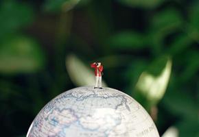 Miniature people photographer figures with camera standing on globe model, travel and photography concept photo