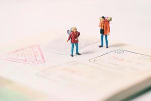 Miniature people figures with backpack walking and standing on passport page with immigration stamps, travel and vacation concept photo