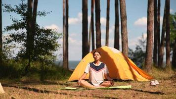 Young woman stretches on a yoga mat outside a yellow tent at camp site video