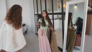 Two young women stand at a full length mirror trying on different outfits video