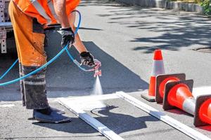 un trabajador de la carretera pinta una señalización vial blanca de un paso de peatones con un aerógrafo en un día soleado. foto