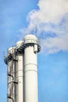 The white triple chimney of a district heating plant emits white smoke into the blue sky. photo