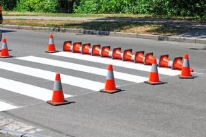 un paso de peatones recién pintado a través de la carretera está cercado con conos de tráfico en un día soleado de verano. foto