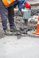 A worker using an electric jackhammer destroys the old asphalt near the sewer manhole. photo