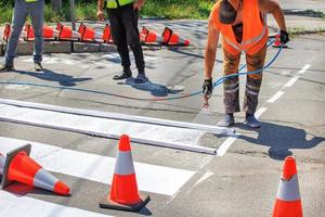 un equipo de trabajadores de la carretera pinta una señalización vial blanca de un paso de peatones utilizando una plantilla de marco de madera y un aerógrafo. foto