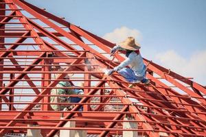 welder workers installing steel frame structure of the house roof at building construction site photo