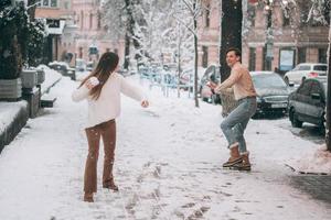 Joyful young couple is playing snowballs at the street. photo