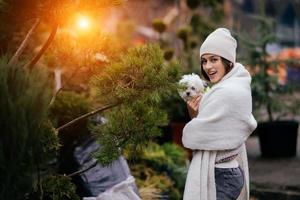 Woman with a white dog in her arms near a green Christmas trees photo