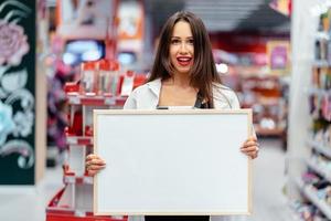 mujer morena sonriente sosteniendo tablero en blanco blanco foto