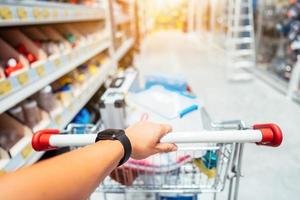 mano humana cerca con carrito de compras en un supermercado caminando por el pasillo foto