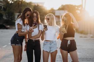 Four attractive women are standing on car parking with smartphones photo