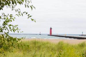 faro en la costa cerca de una playa de arena blanca en el lago michigan. escondido detrás de la hierba alta y un árbol hay un faro rojo en un muelle en kenosha, wisconsin, detrás de un muro de ruptura foto