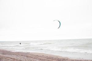 Single kite surfer on stormy waters of Lake Michigan. Sandy beach on the edge. Small pebbles along the shoreline line. Cloudy overcast sky. Colorful parachute. photo