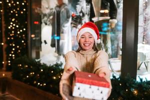 Young woman giving box for you outdoor. Gift exchange concept. photo