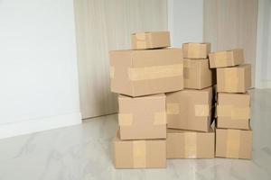 pila de cajas de cartón para mudanzas, habitación vacía con una pared blanca y cajas de cartón con código de barras sin marca en el suelo. entrega de mercancías, compras. cajas de cartón sobre fondo de pared gris. foto