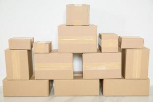 pila de cajas de cartón para mudanzas, habitación vacía con una pared blanca y cajas de cartón con código de barras sin marca en el suelo. entrega de mercancías, compras. cajas de cartón sobre fondo de pared gris. foto