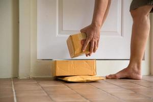 Woman collects parcel at door. box near door on floor. Online shopping, boxes delivered to your front door. Easy to steal when nobody is home. Parcel in cardboard box on doorstep. Delivery service photo