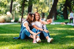 Two female friend sitting in the park have a rest take a selfie photo
